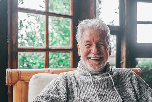 Senior man in grey sweater sitting in chair and smiling