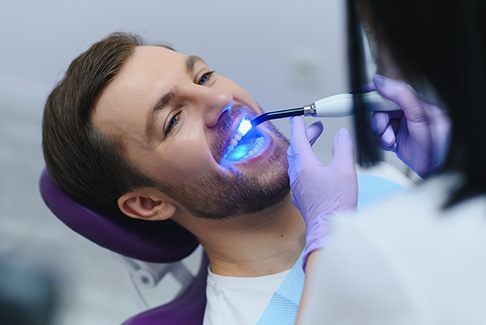 Dentist applying UV light to man’s dental bonding