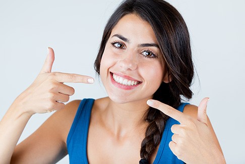 Woman wearing blue pointing to her smile with both hands