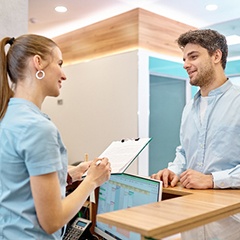 Male patient smiling while talking to dental receptionist about cost
