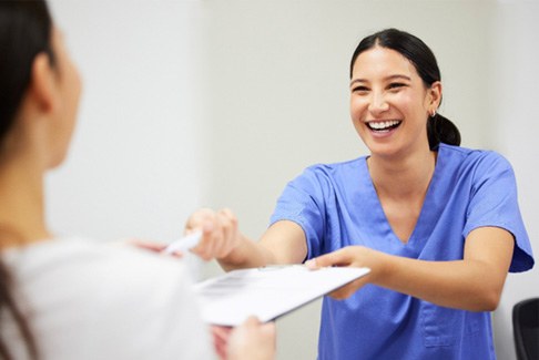a dental assistant handing a form on a clipboard to a patient