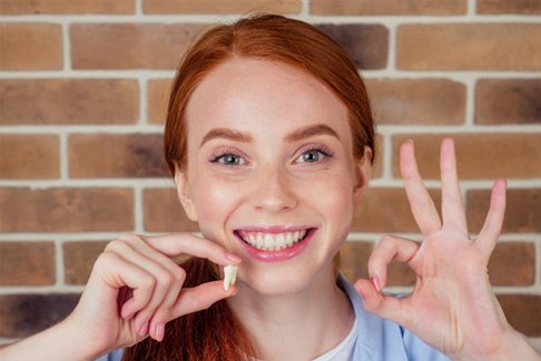 A smiling redhaired girl holding an extracted tooth