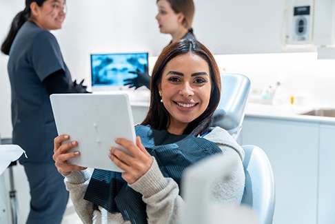 Patient smiling while holding mirror in treatment chair