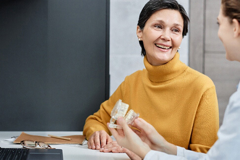 woman in an orange sweater talking to a dentist holding model teeth