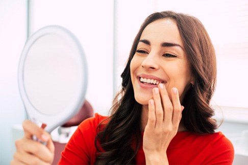 Woman checking smile in mirror after getting dental implants in Sterling Heights, MI
