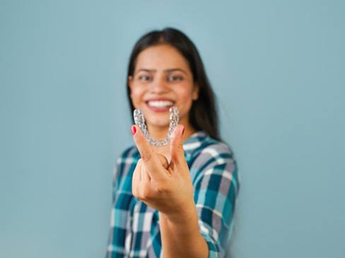 Smiling woman in plaid shirt holding Invisalign aligner