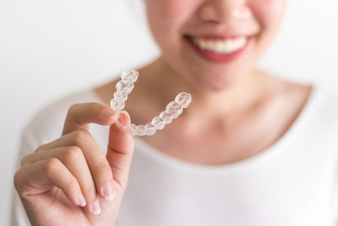 Smiling person holding up an Invisalign tray