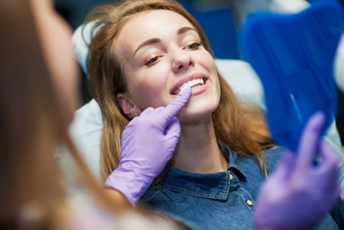 Woman looking at smile in mirror after tooth extractions