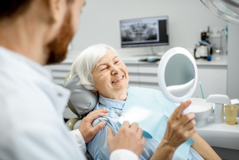Woman with dentures looking at her smile in the mirror
