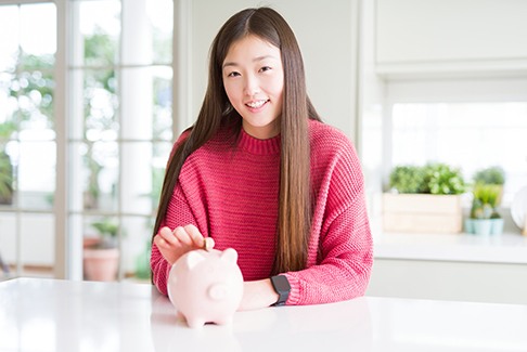 Patient in Sterling Heights smiling while putting a coin in piggy bank