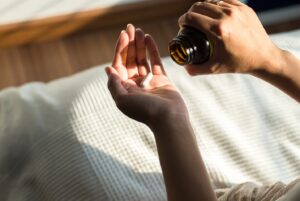 Person shaking one vitamin into their palm out of pill bottle.
